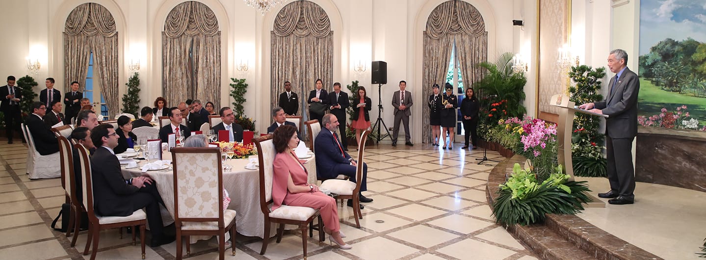 Lee Hsien Loong at podium in suit speaking to seated audience in a formal hall.